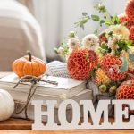 Autumn still life with a bouquet of chrysanthemum flowers, the decorative word home and pumpkins on a blurred background.